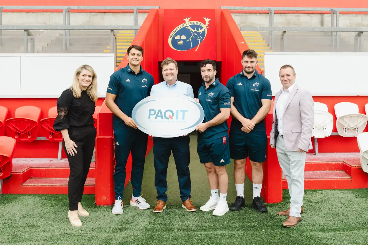 6 people stood in a line, middle person holding a PAQIT logo.