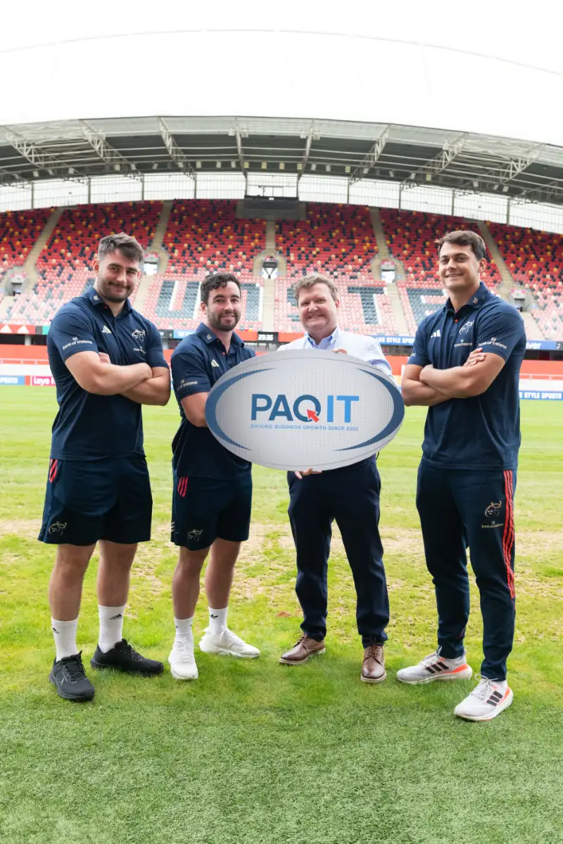 PAQ IT team standing on rugby pitch holding paq branded sign
