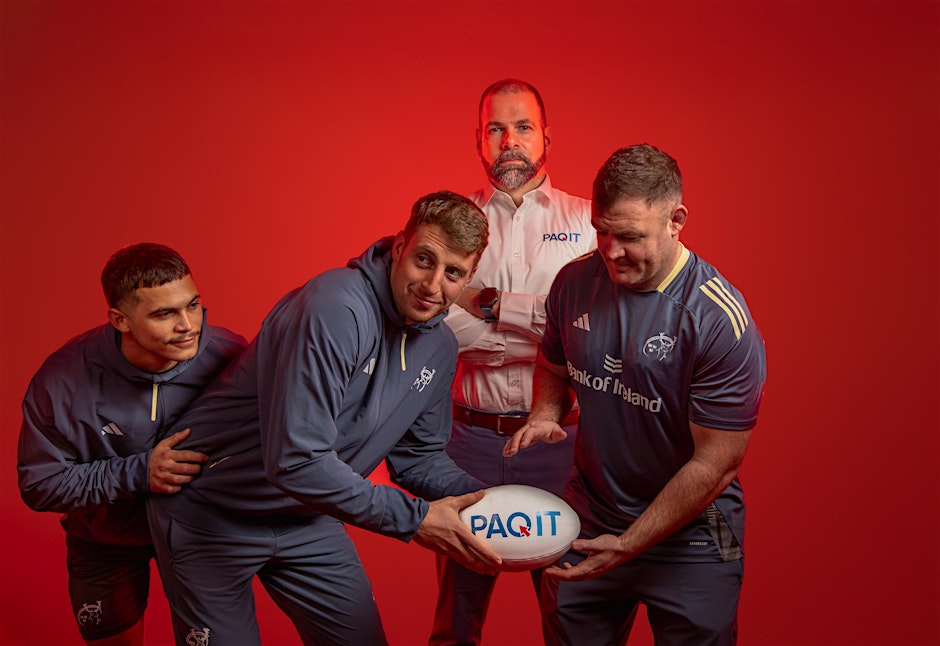three rugby players holdng rugby ball with PAQIT logo on, man stood in background wearing PAQIT uniform.